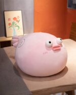 Pink pufferfish plush toy sitting on a table, soft and cute.