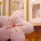 Pink sakura flower pillow displayed on a shelf with floral artwork.