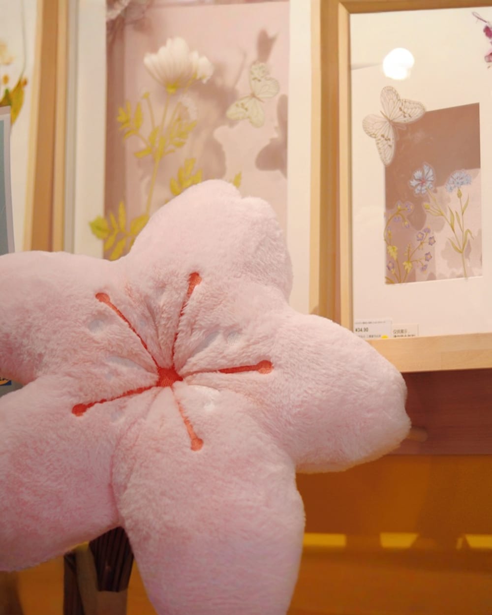 Pink sakura flower pillow displayed on a shelf with floral artwork.