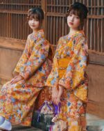 Two women wearing a flower summer yukata with a vibrant yellow and orange floral pattern.