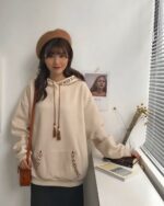 Cream colored ethno-chic hoodie worn by a woman, featuring embroidered details and tassels.