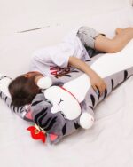 Long cat plushie, Whiskers the Stripped Emperor Cat, resting on a bed.