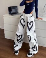 White y2k aesthetic pants with black heart spray paint details. High-waisted loose fit.