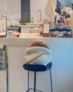 A brown mushroom homunculus plushie rests on a cafe bar stool.