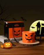 Orange Halloween pumpkin cup with black handle, surrounded by Halloween decorations.