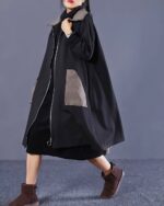 Black long hooded coat worn by a model, featuring a layered design and zippered details.