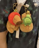 Two Turtle Backpack Capybara plushies hang on a backpack, featuring strawberry and turtle designs.
