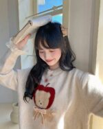 Woman wearing a cottagecore bear sweater with an apple design.