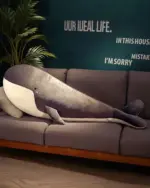 Large kawaii whale plushie, Bubbles, resting on a gray sofa with a potted plant in the background.