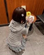Woman wearing a jojifuku aesthetic hoodie, holding plush toys at a table.