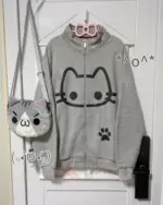 Cute Neko print hoodie displayed with a gray zippered jacket, crossbody bag, and accessories.