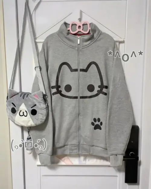 Cute Neko print hoodie displayed with a gray zippered jacket, crossbody bag, and accessories.