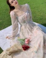 Woman wearing a delicate french floral dress with long sleeves, resting on a picnic blanket.