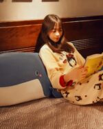 A girl cuddling a kawaii whale plushie and reading a book.