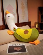 Soft yellow banana duck plushie with orange feet and beak, resting on a bed.