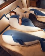 Blue and white kawaii whale plushie resting on a bed with a person.