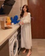 Woman wearing a white soft girl aesthetic nightdress, holding a mug, in a kitchen setting.