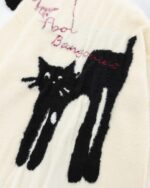 Close-up of a cat embroidered sweater featuring black cat designs on a beige knit fabric.