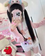 Person wearing a kawaii striped shirt and plush toys in a pink bedroom setting.