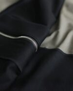 Close-up of a long hooded coat featuring a zipper detail and layered fabric.