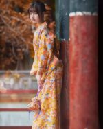 Woman wearing a flower summer yukata, featuring a vibrant floral pattern in shades of orange and yellow.