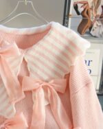 Close-up of a dollcore pink sweater with bow accents, showcasing its knitted texture and design.
