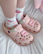 Pink Piggy Crocs with pig decorations on a white bedspread.
