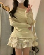 A beige one-shoulder knitwear sweater paired with a ruffled skirt.