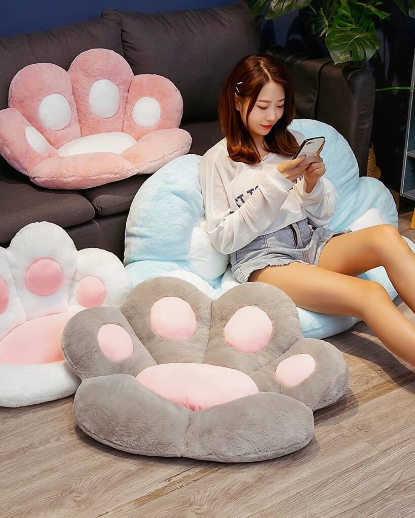 Kawaii Neko Paw Cushion, a plush, grey paw-shaped pillow with pink accents, displayed on a sofa.