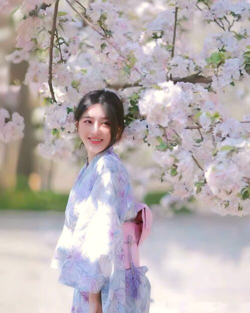A woman wearing a pastel japanese yukata outdoors amidst cherry blossoms.