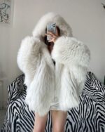 White puffy hooded coat with faux fur trim, displayed on a patterned sofa.