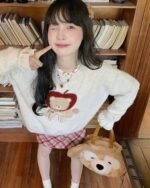 Woman wearing a cottagecore bear sweater with an apple design, holding a plush bear.