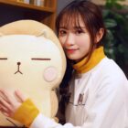 A catoast plushie sits next to a woman indoors.