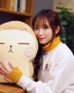 A catoast plushie sits next to a woman indoors.