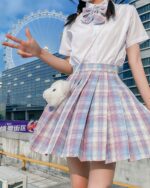 Pink and white jk plaid skirt with white blouse and bow, outdoors.