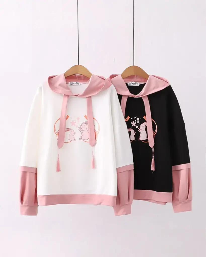 Two sakura bunny hoodies, one white with pink trim and one black with dark trim, hanging on a rack.