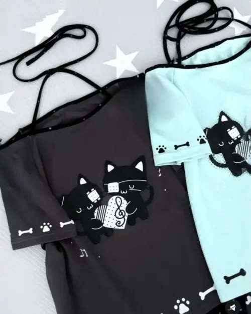 Two off-shoulder black cat t-shirts, one black and one teal, feature a musical cat design.