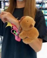 Close-up of a brown capybara plushie bracelet held on a person's wrist.