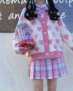 Close-up of a kawaii knitted sweater with heart pattern, layered with a pink pleated skirt.