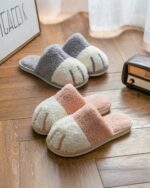 Pair of plush cat paw slippers in beige, white, and pink colors on wooden floor.