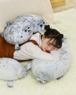 Two Yuki the Seal Plush toys displayed on a rug, with a person resting among them.