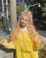 A woman wearing a yellow vintage banana sweater with banana illustrations, posing outdoors.