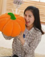 Large orange pumpkin plush cushion held by a woman, aesthetic room decor.