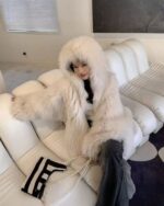 Woman wearing a fluffy, puffy hooded coat in a modern interior.