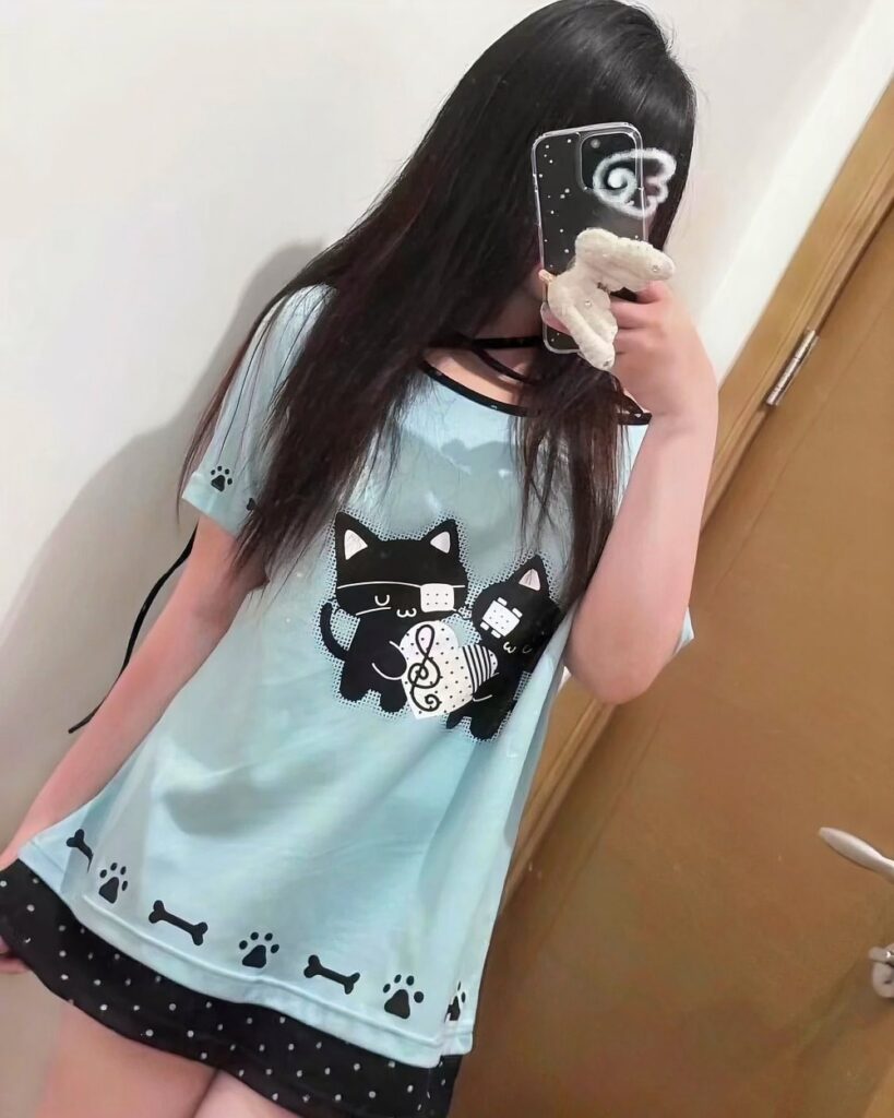 Model wearing a light blue off-shoulder black cat t-shirt with black cat and paw details.
