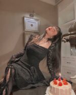 Black lace gothic aesthetic dress worn by a woman, sitting with a cake.