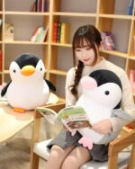 Two Pip and Family penguin plushies sit next to a girl reading a book.
