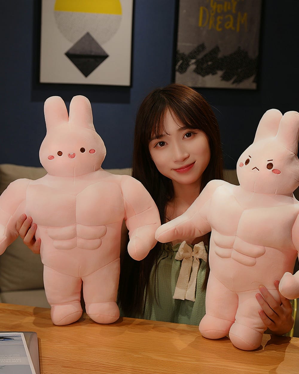 Two pink buff bunny plushies displayed on a table. One is held by a woman.