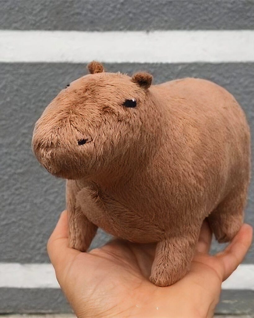 Brown capybara plushie in hand against a striped background.
