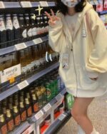 Woman wearing a white puppy hoodie in a supermarket aisle.